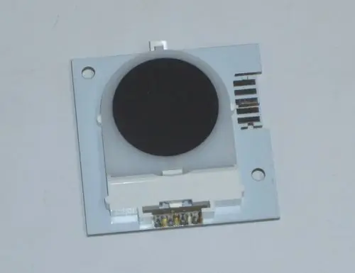 Schwarze runde Linse auf einer weißen Platine mit Anschlüssen, möglicherweise Teil eines Daikin-Produktes.